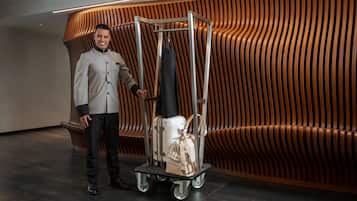 A person standing next to a luggage cart with suitcases and a handbag.