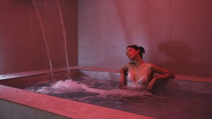 Una mujer en una bañera con agua cayendo de un cabezal de ducha.