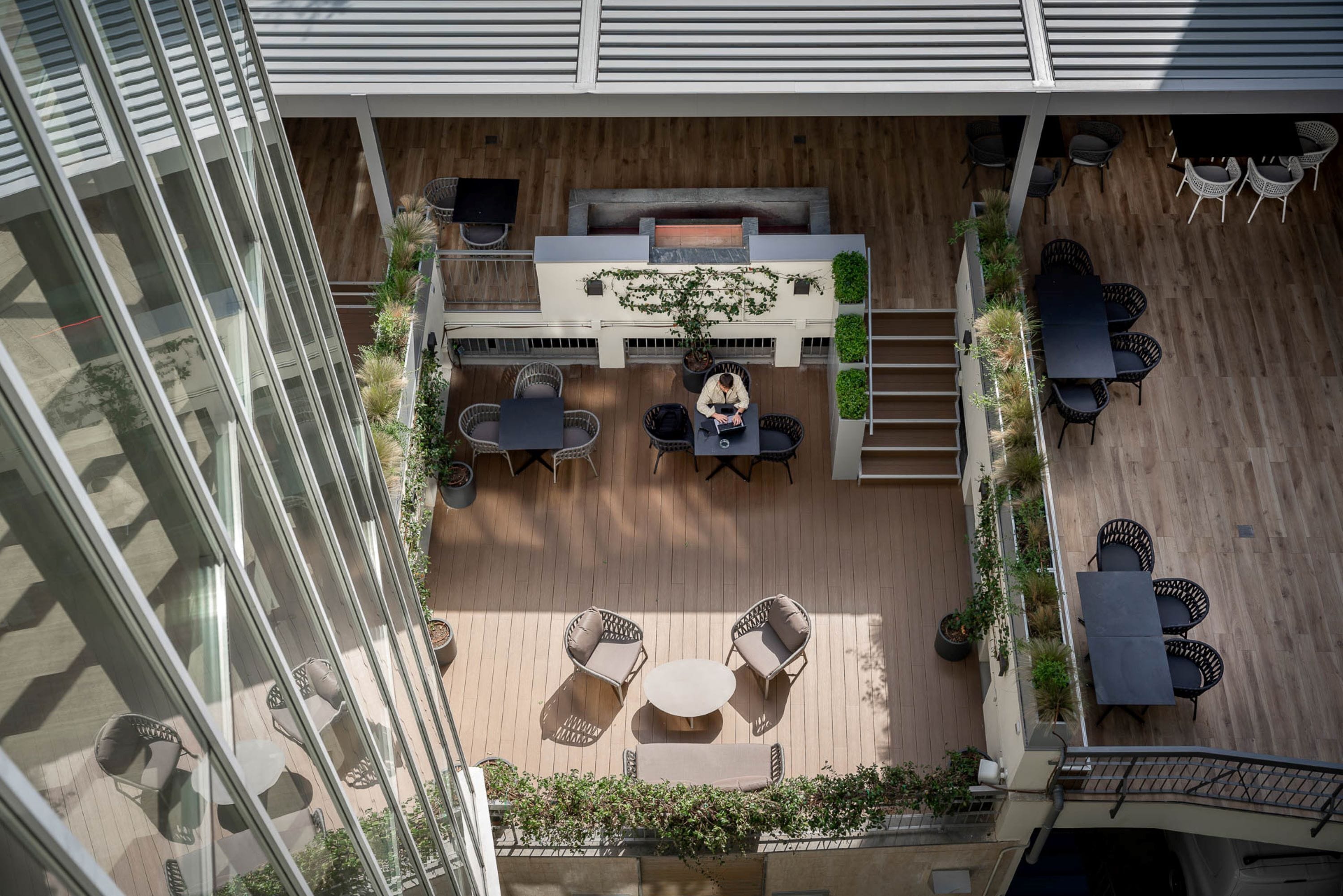 Vista aérea de un patio en la azotea con mobiliario exterior, una mesa central y una escalera que conduce a un nivel superior.