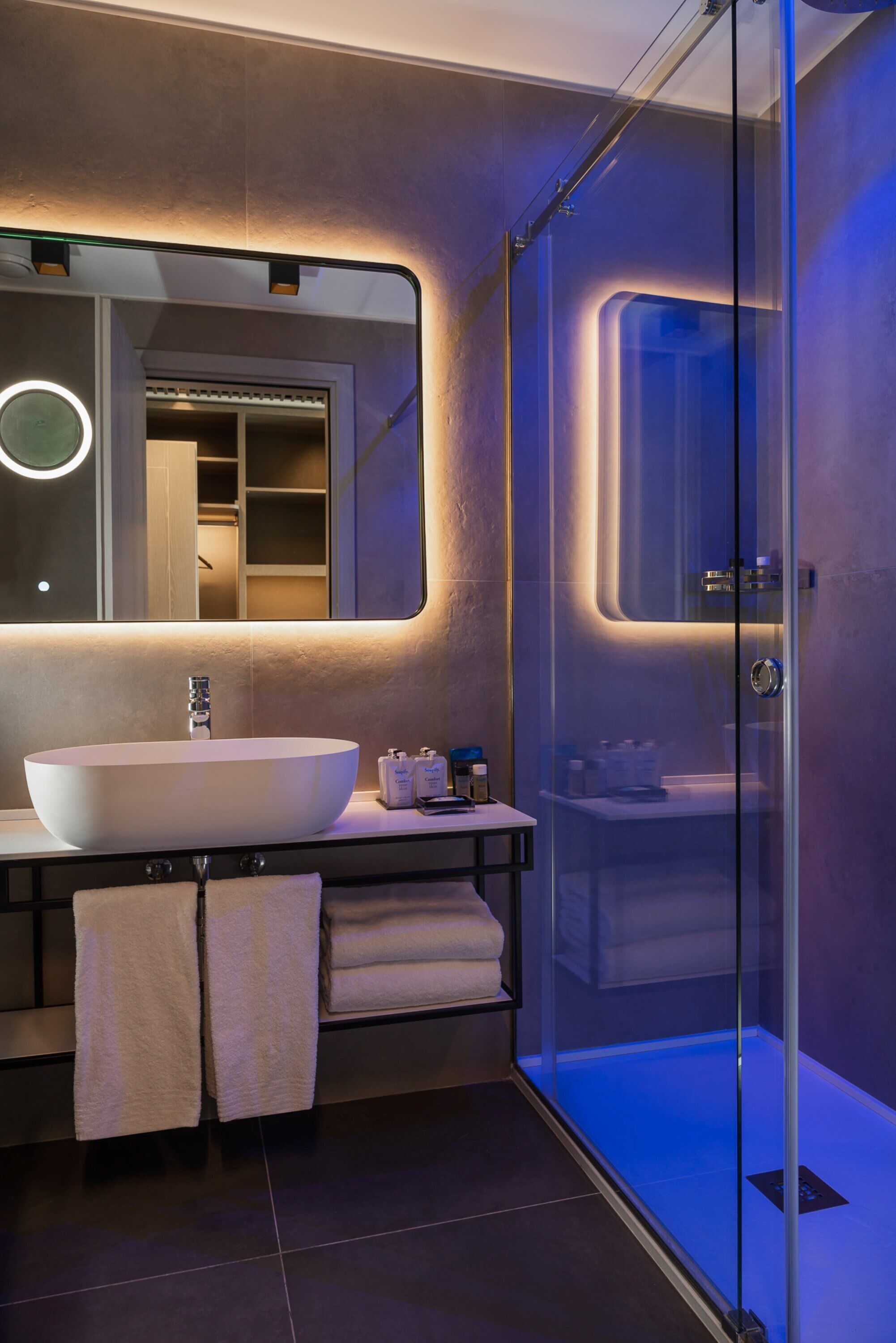 Un bagno moderno con un ampio lavabo ovale, cabina doccia in vetro e uno specchio con illuminazione integrata.