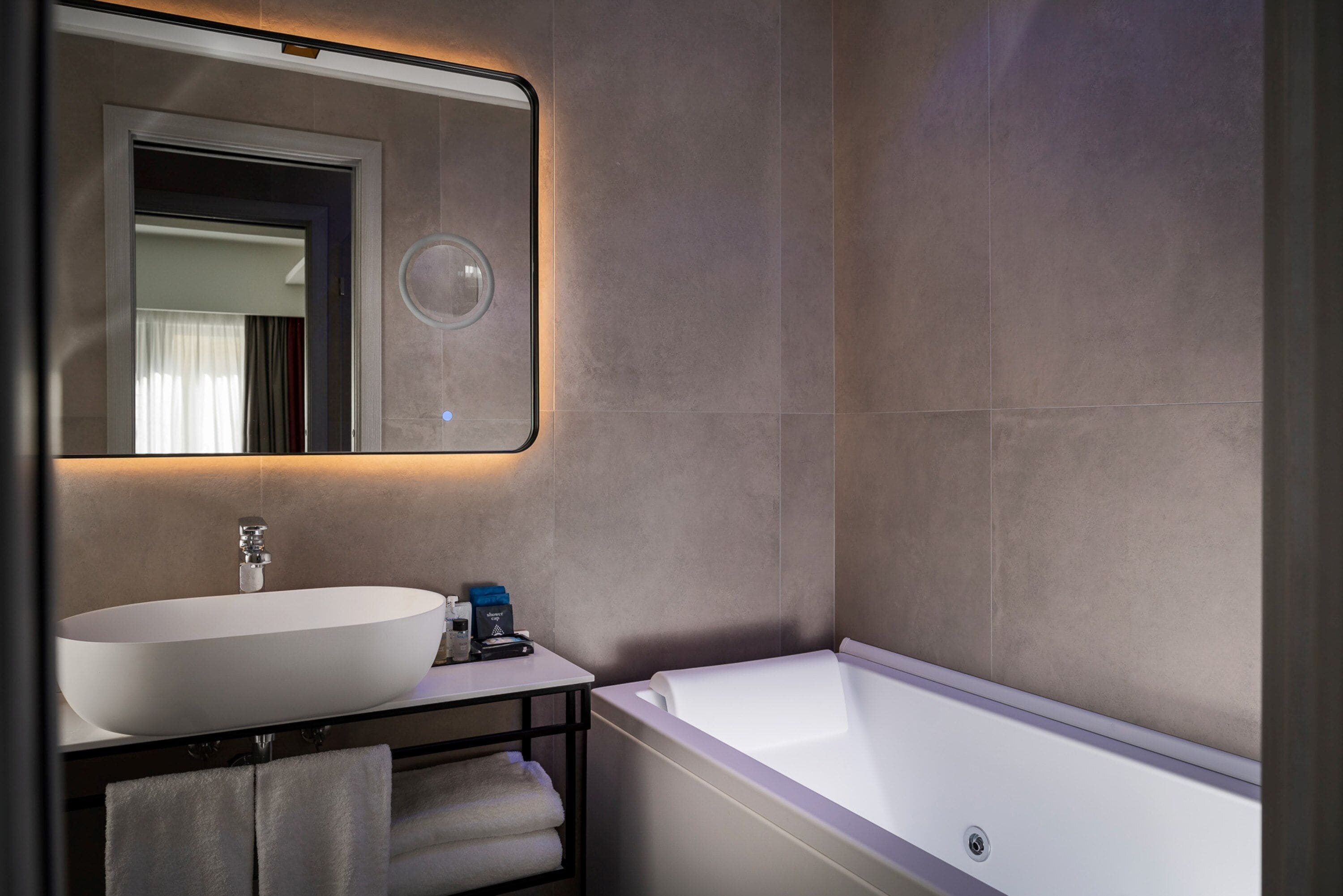 A modern bathroom with a large oval sink, a bathtub, and a mirror with integrated lighting.