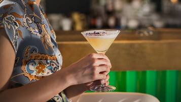 Una persona che sorseggia un martini al bancone di un bar, con sullo sfondo sfocato bottiglie e bicchieri.