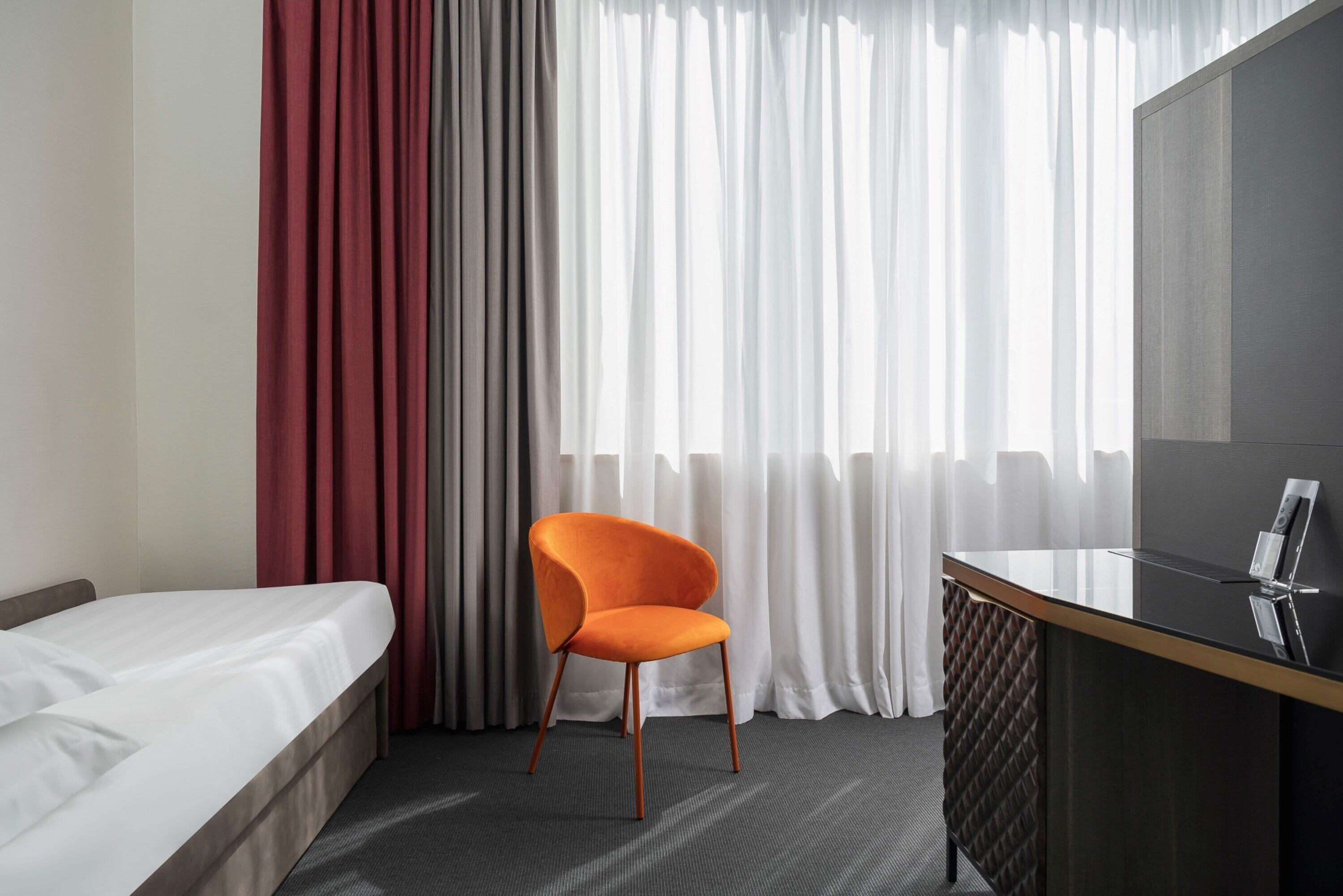 Una camera d'albergo con un letto, una scrivania, una sedia e un'ampia finestra con tende.