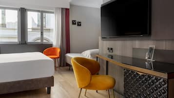 Ein modernes Hotelzimmer mit einem Bett, einem Schreibtisch mit Flachbildfernseher, einem Sessel und Blick auf die Stadt durch große Fenster.