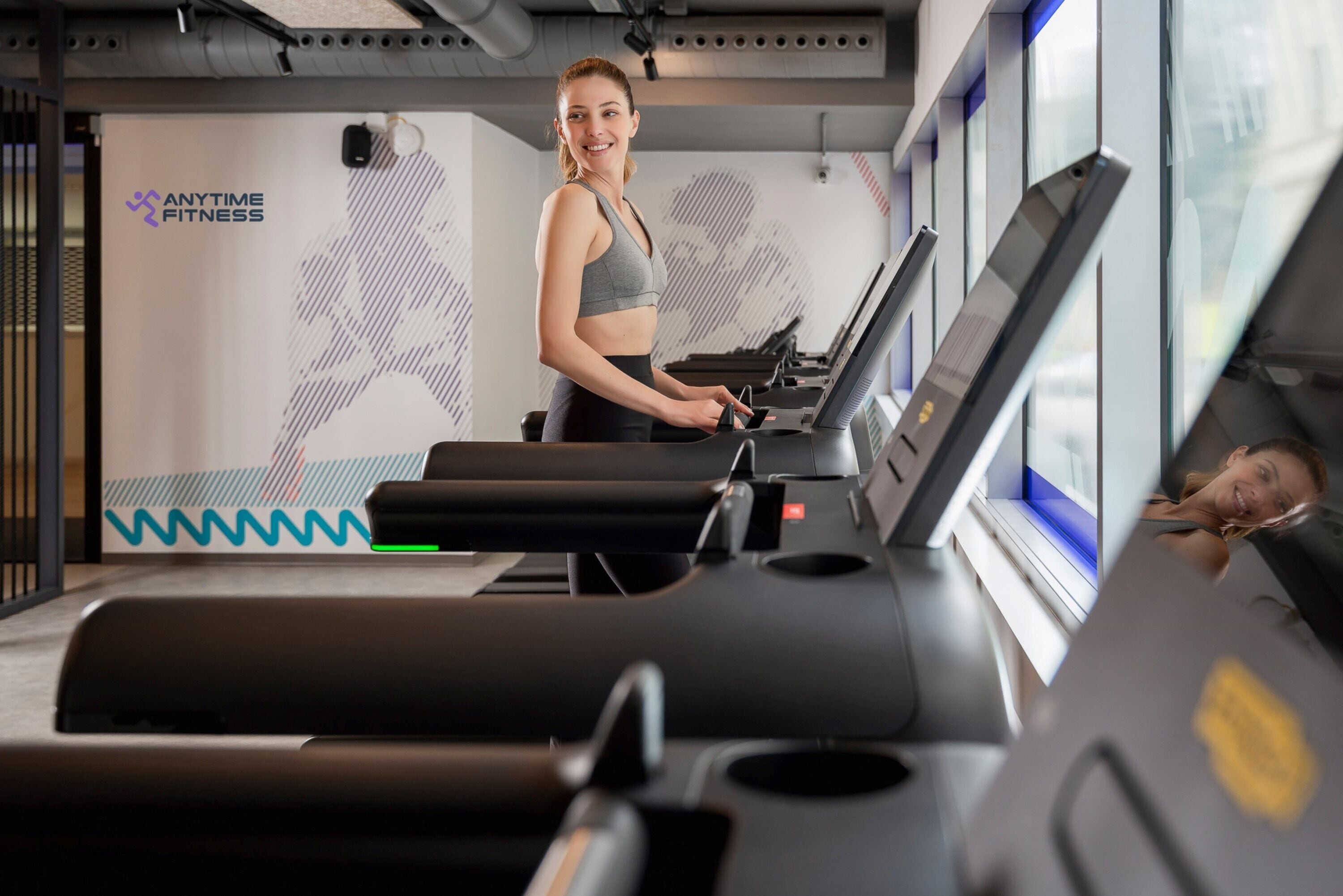 A gym with treadmills, a logo on the wall, and a window with a view.