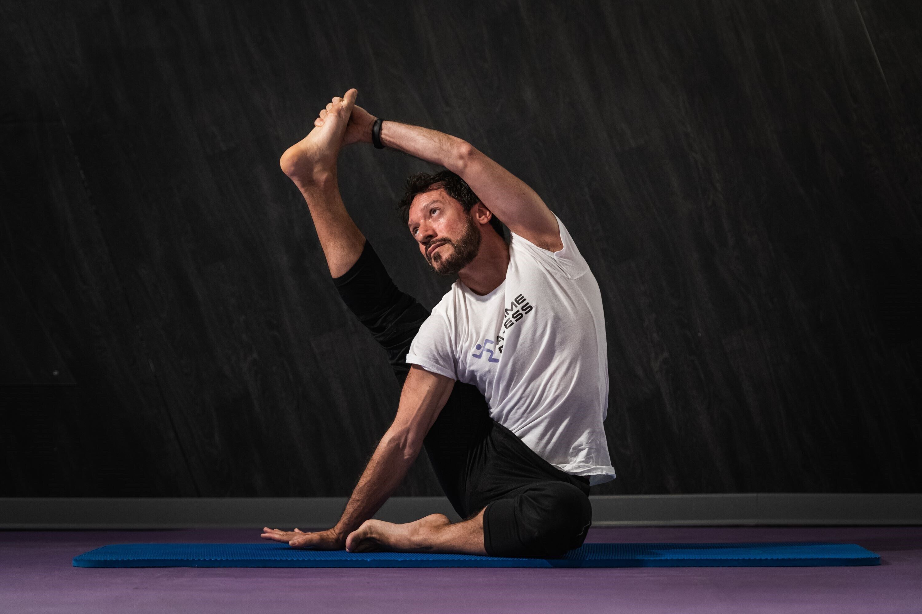 Une personne effectuant une posture de yoga sur un tapis bleu, le tout se détachant sur un fond sombre.