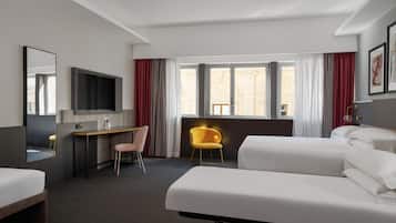 A hotel room with a bed, a desk, a chair, a TV, and a window with curtains.