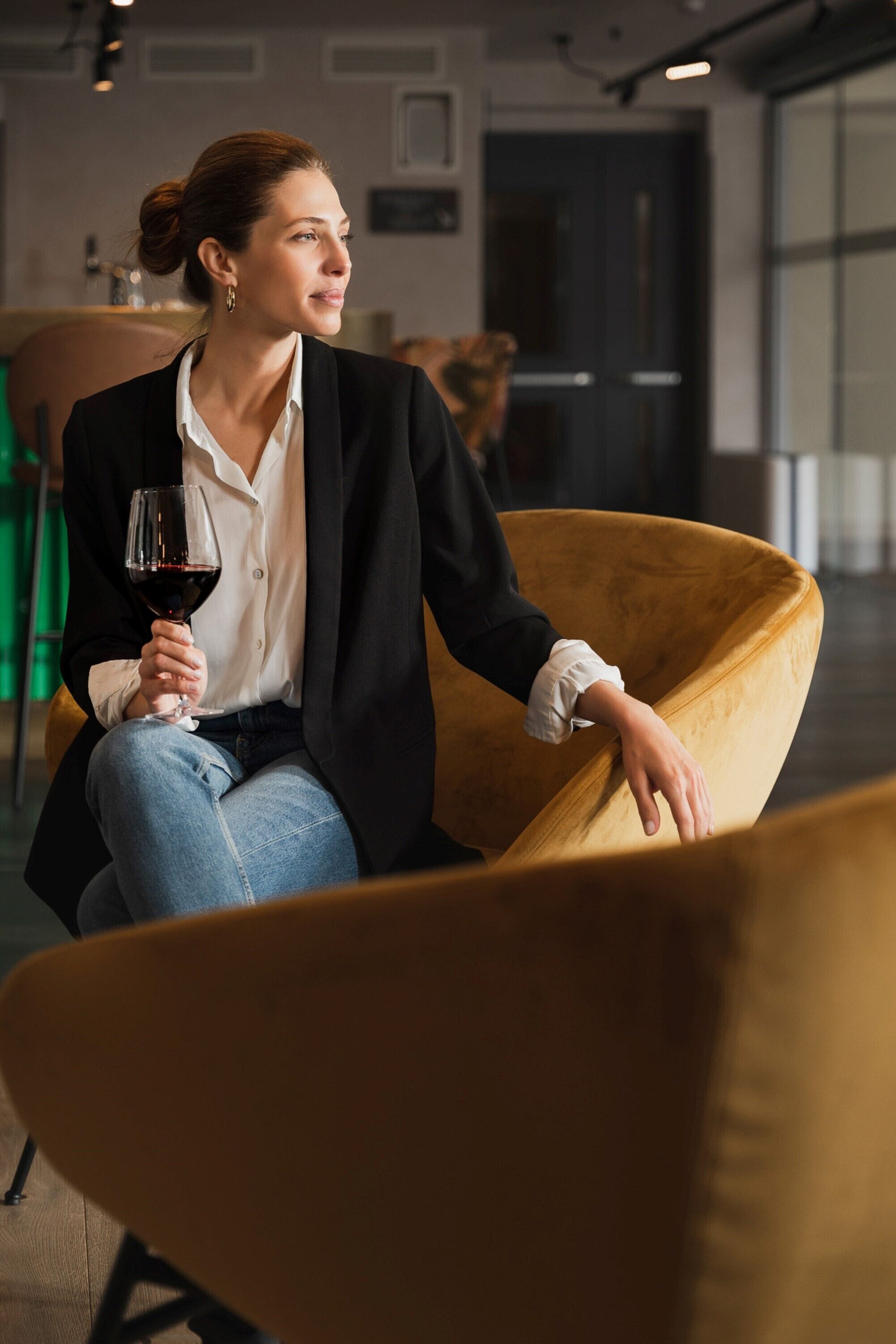 Eine Person sitzt auf einem gelben Stuhl und hält ein Glas Rotwein.