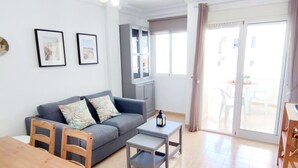 Ein modernes Wohnzimmer mit einem grauen Sofa, Holzstühlen, einem kleinen Tisch und einem Schrank.
