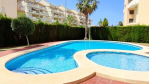 Ein Pool mit geschwungener Form, umgeben von einem Heckenwall und einem Gebäude mit Balkonen.