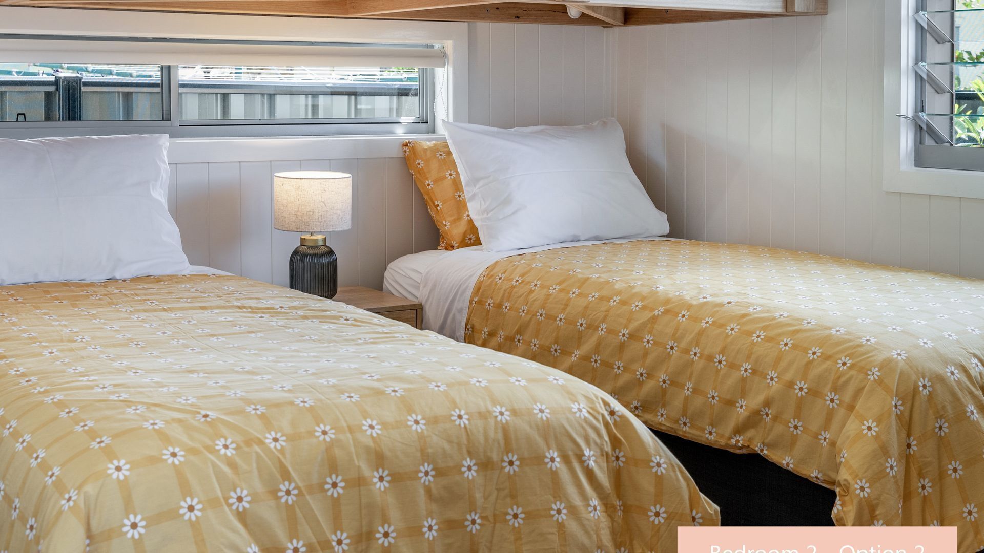 Un dormitorio con dos camas, una mesita de noche, una lámpara y una ventana con persianas.