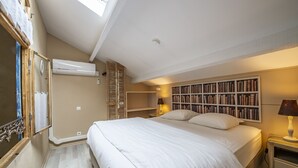 Ein Schlafzimmer mit einem großen Bett, einer Klimaanlage, einem Bücherregal und einem Nachttisch mit Lampe.
