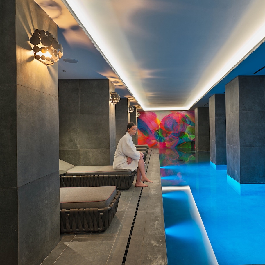A modern spa area with a blue-lit pool, a colorful mural, and a seating area with a person.