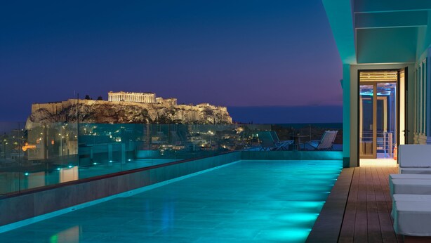 A rooftop pool with a view of a historic building and a cityscape at dusk.