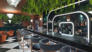 A bar area with a modern design, featuring a bar counter, seating with bar stools, and a chandelier.