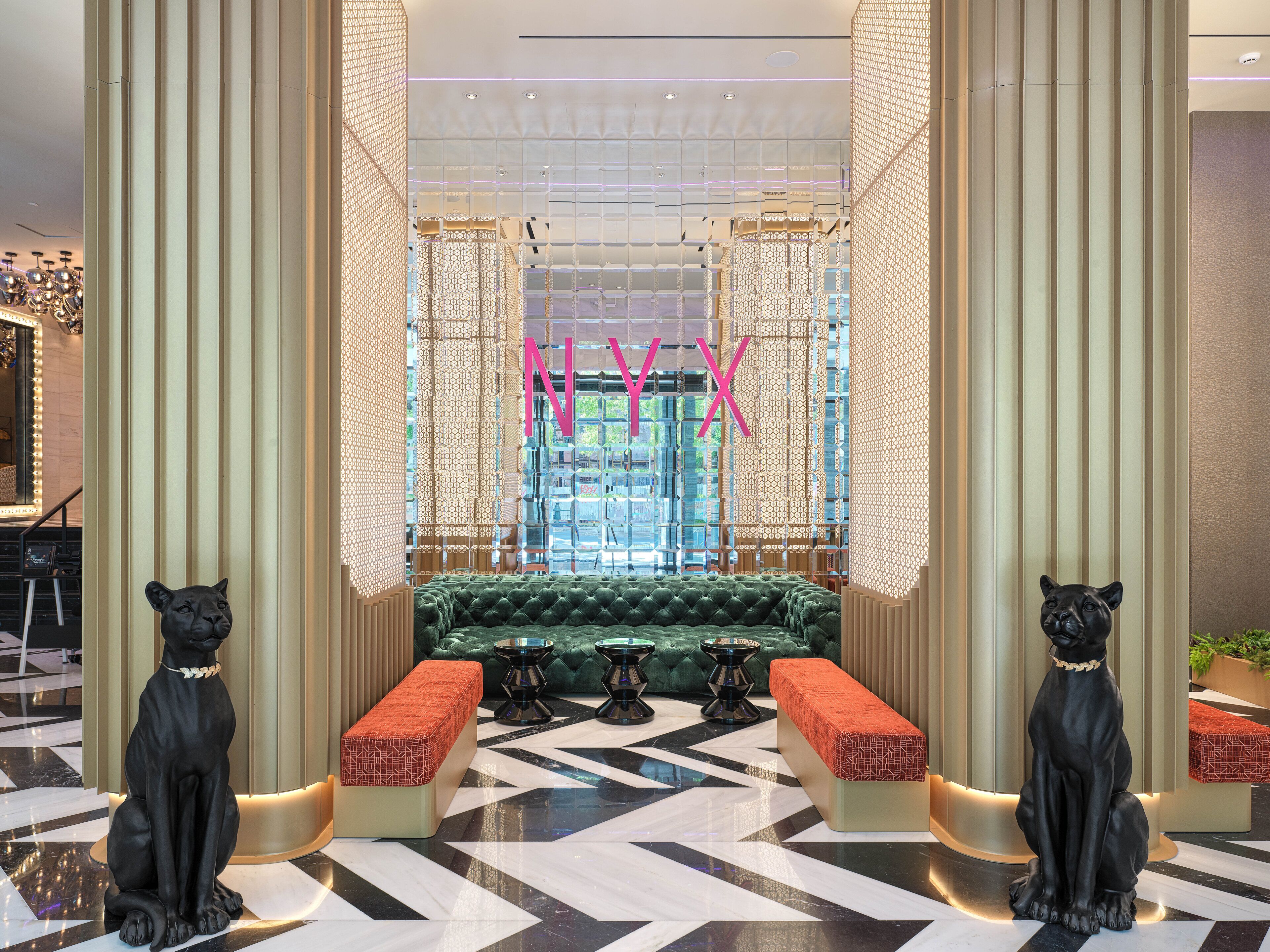 A lobby with a geometric patterned floor, a green upholstered bench, and two black dog statues.