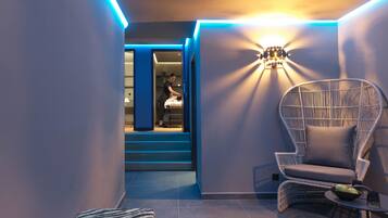 Een modern interieur met een zithoek, bestaande uit een rieten stoel, een klein tafeltje met een schaal en een glas, en een trap die naar een andere kamer leidt.