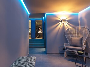 A modern interior with a lounge area featuring a wicker chair, a small table with a bowl and a glass, and a staircase leading to another room.