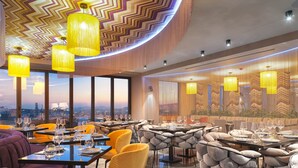 A modern restaurant with high tables, yellow chairs, and large windows offering city views.