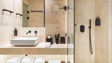 Un baño moderno con un lavamanos grande de color blanco, una cabina de ducha con mampara de vidrio y toallas ordenadas sobre una repisa de madera.