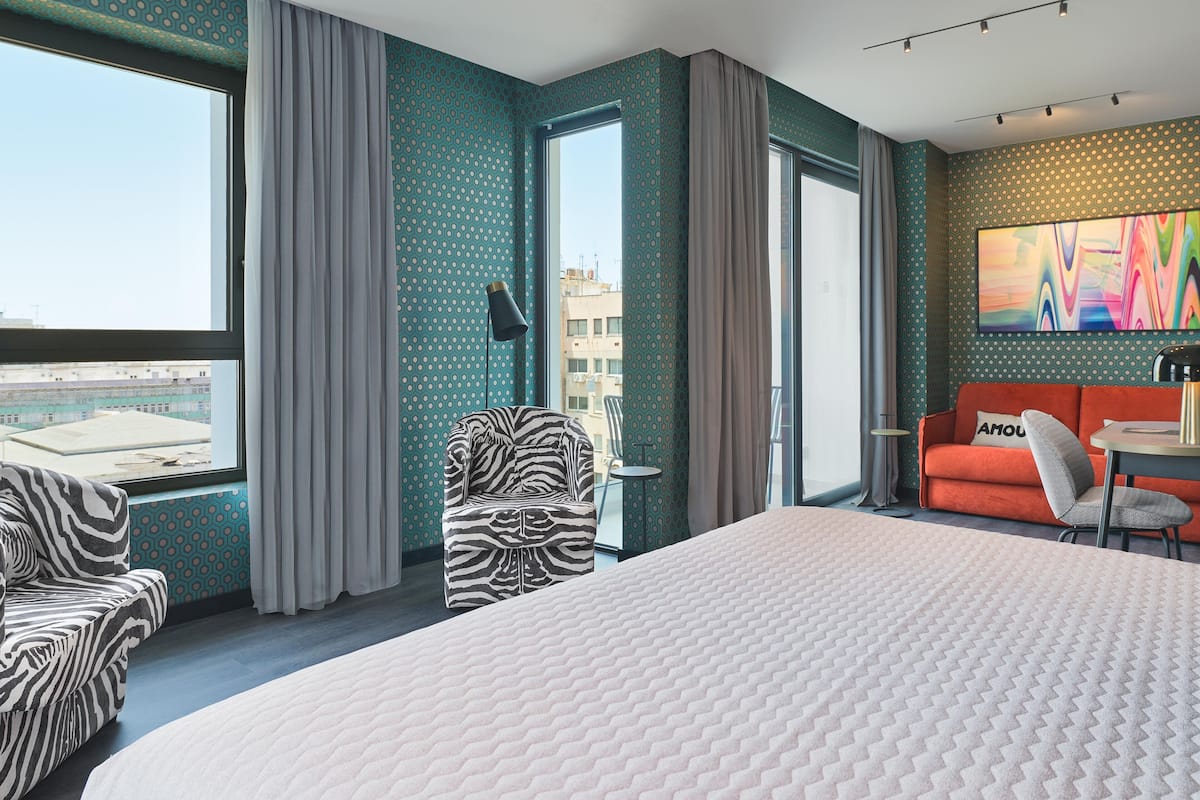 Ein Hotelzimmer mit einem großen Bett, einem zebra-gestreiften Sessel, einem kleinen Tisch und einer Couch mit Kissen.