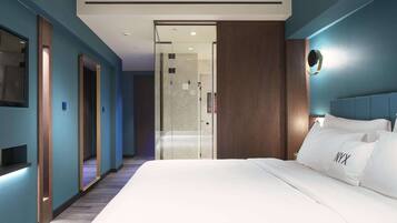 A modern hotel room with a large bed, a glass door leading to a bathroom, and a blue accent wall.