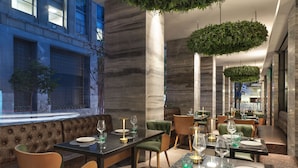 A modern restaurant with a long dining area, cushioned seating, and a view of the cityscape.