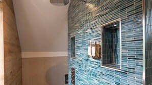 Een moderne badkamer met een wand betegeld met mozaïek, een douchegedeelte en een houten vloer.