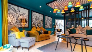 Un salon moderne avec un mur d’accent de couleur turquoise, un canapé jaune, un pouf à carreaux et un tapis gris.