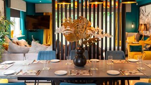 Un coin repas avec une table dressée pour quatre personnes, un vase rempli de fleurs et un intérieur moderne aux murs turquoise et aux suspensions noires.