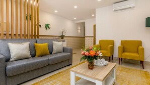 Un salón moderno con un sofá gris, sillones amarillos, una partición de madera y una mesa de centro blanca con un centro de mesa floral.