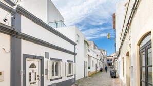 Una estrecha calle adoquinada flanqueada por edificios blancos, con una mezcla de viviendas y locales comerciales.