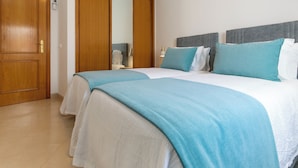 Habitación de hotel con dos camas, una puerta de madera, un espejo y una mesita de noche con lámpara.