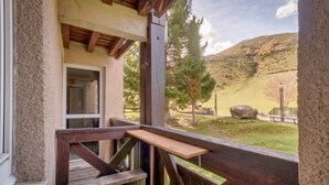 A wooden deck with a bench and a small table, overlooking a grassy area with trees and a hill in the background. - Chalet atmosphere for 4 - 80m from the slopes (Genos)