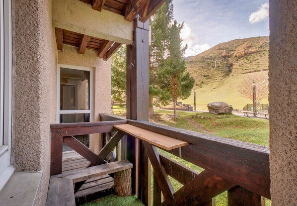 A wooden deck with a bench and a small table, overlooking a grassy area with trees and a hill in the background.
