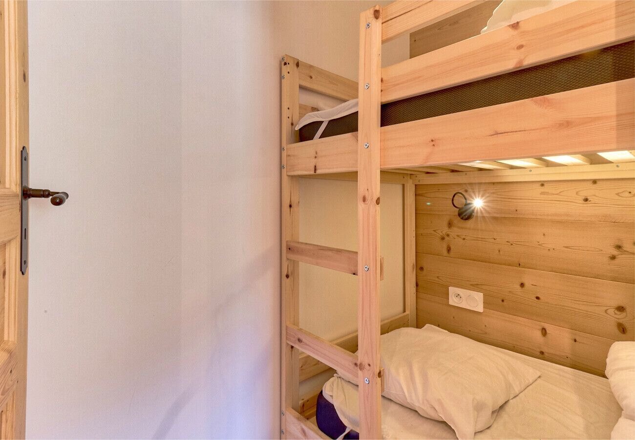 A bunk bed with a wooden frame and a headboard, a door with a handle, and a light fixture on the wall.
