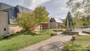 A building with a sign indicating it is a sports facility, a paved pathway, and a stone monument. - Chalet atmosphere for 4 - 80m from the slopes (Genos)