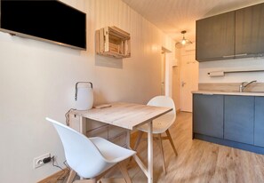A compact kitchen with a wooden table and white chairs, a built-in sink, and a TV mounted on the wall.