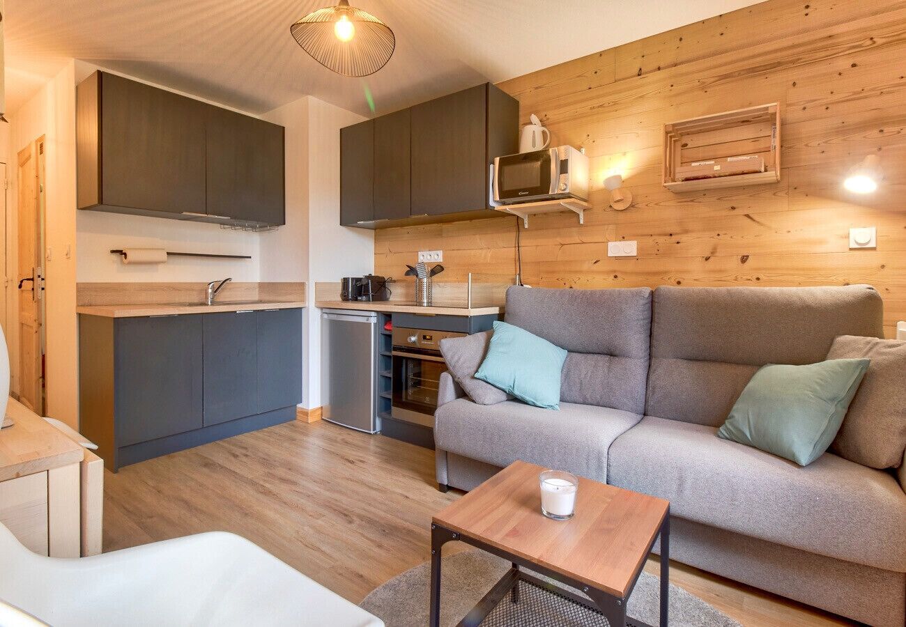 A compact living space with a kitchenette, grey sofa, and a small wooden table.