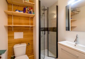 A bathroom with a toilet, a glass-enclosed shower, a sink, and wooden shelves above the toilet.