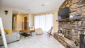 A living room with a stone fireplace, a sofa, a chair, and a television.