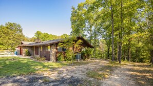 A rustic cabin with a stone exterior, a wooden deck, and a gravel driveway.
