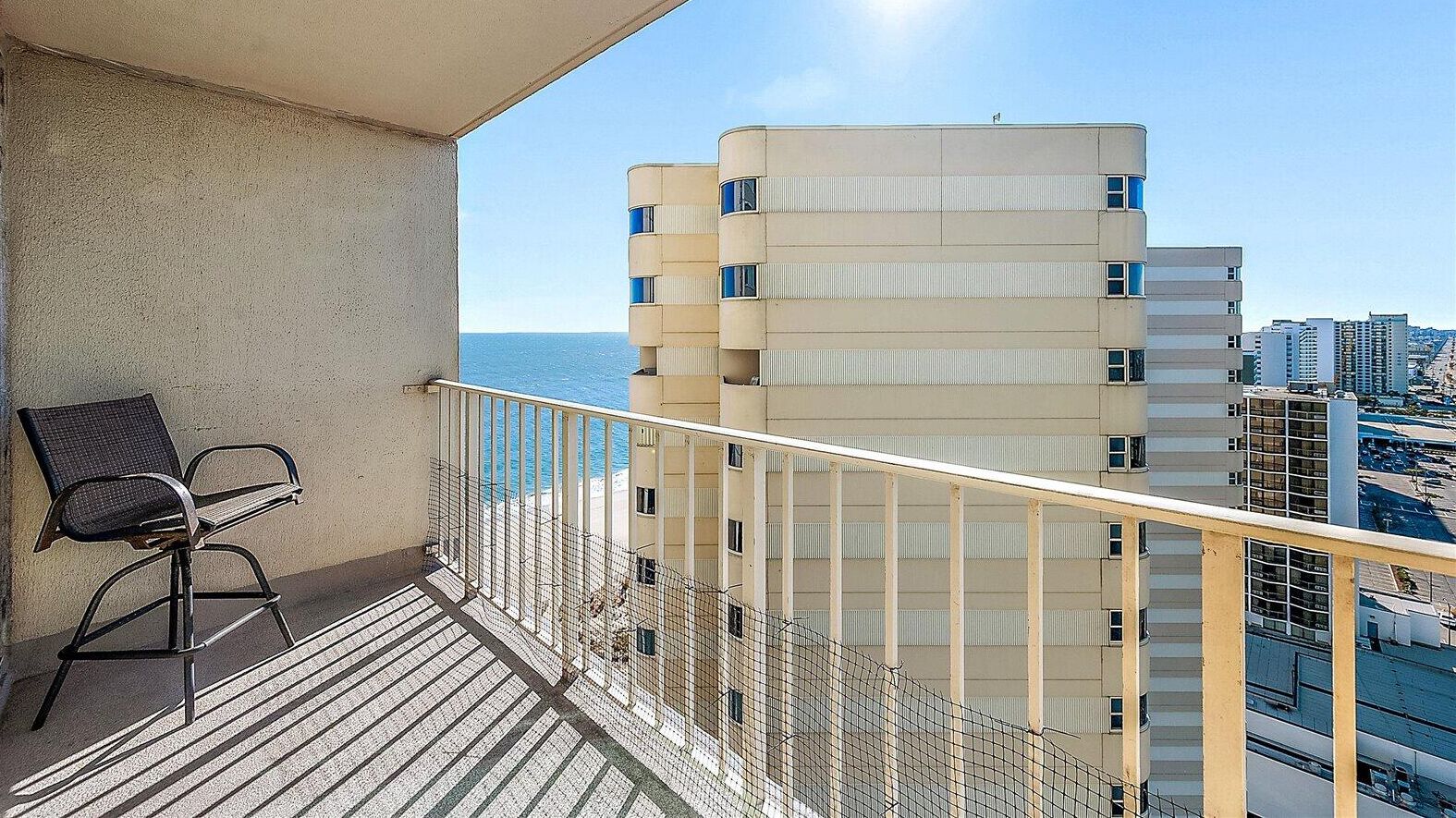 Un balcón con una silla, barandilla y vistas de un edificio alto con múltiples ventanas.