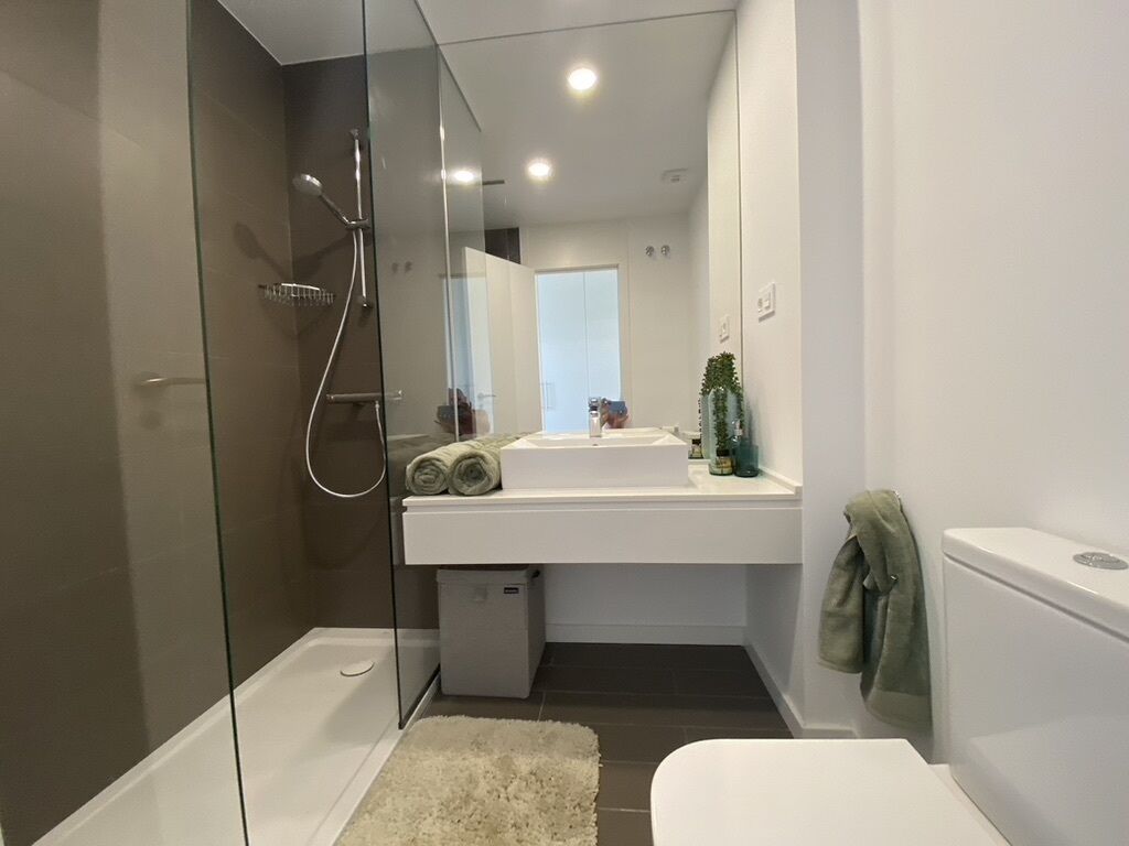 Een moderne badkamer met een douchecabine van glas, een witte wastafel en een toilet.