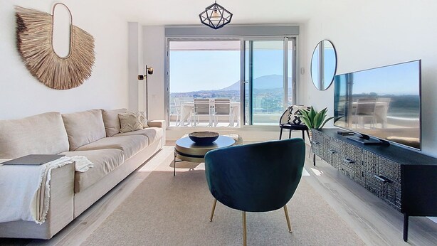 A modern living room with a sofa, a round table, a dark chair, a TV, and a large window with a view of a mountain. - ALL COMFORT, SUPERB VIEW, large TERRACE Los Flamingos Ideal families (Estepona)