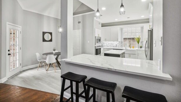 A modern kitchen with a large island, white cabinets, and pendant lighting. - Modern, Spacious - Pool & Backyard Oasis & Cinema (Rowlett)