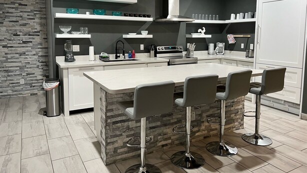 A modern kitchen with a central island, bar stools, and a stone accent wall. - Lovely white & Grey home (Buckeye)
