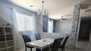 A dining area with a white table and four chairs, a white bookshelf, and a window with blinds. - Lovely white & Grey home (Buckeye)