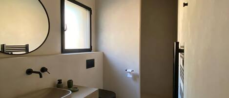Un baño moderno con un espejo grande, un lavamanos y una ventana.