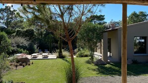 Een houten terras met een pergola erboven, een gazon en een modern gebouw op de achtergrond.
